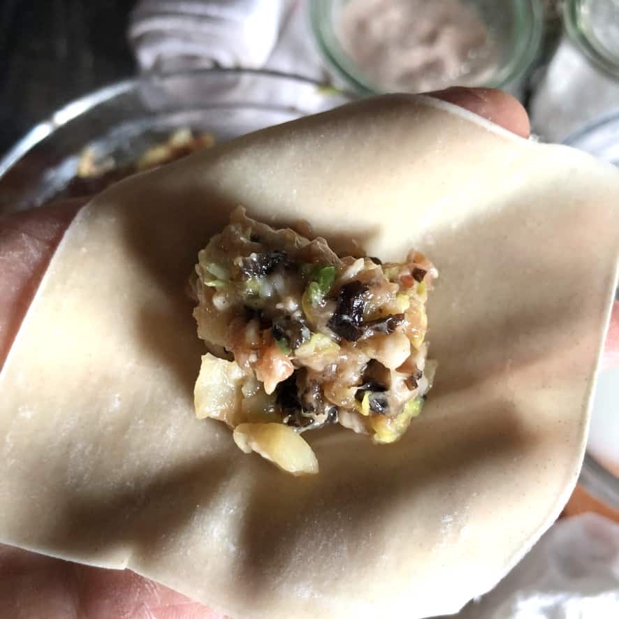 my hand holding a wonton wrapper with pork filling in the middle of it