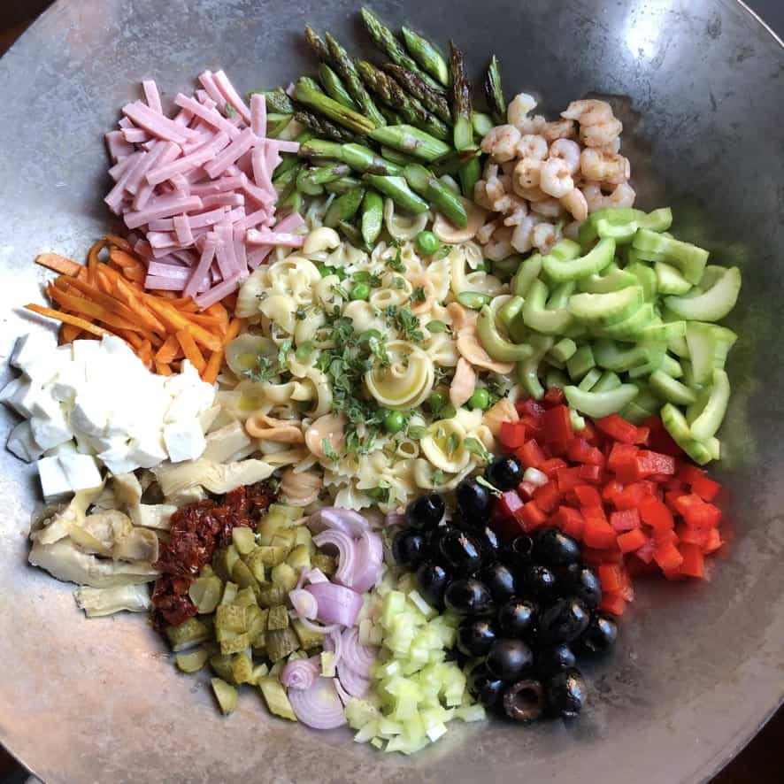 Mediterranean pasta salad components all bundled together in a wok before being stirred together.