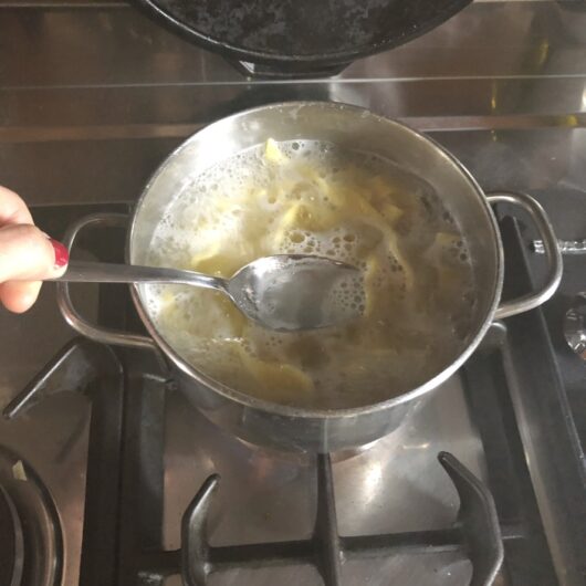 a ladle full of starchy cooking water above the pot with cooking bigoli pasta