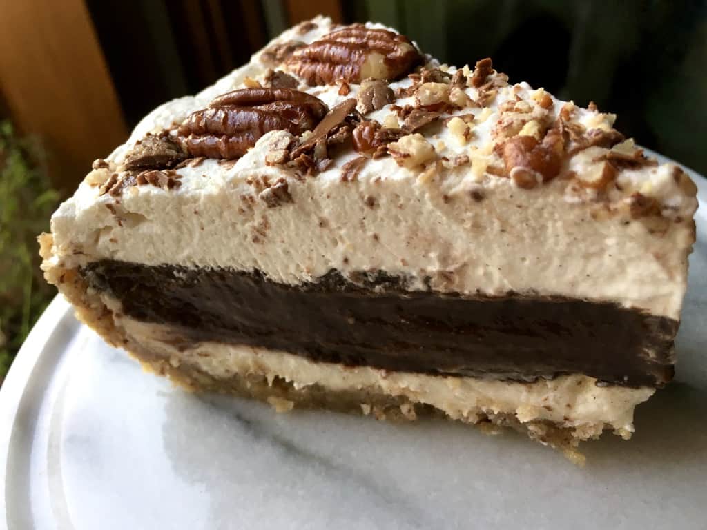 slice of arkansas possum pie with cream cheese layer, scratch made chocolate pudding layer, pecan shortbread crust layer, and whipped cream layer