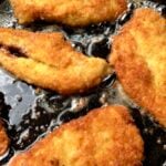 Golden crispy chicken cutlets being shallow fried in a cast iron skillet.