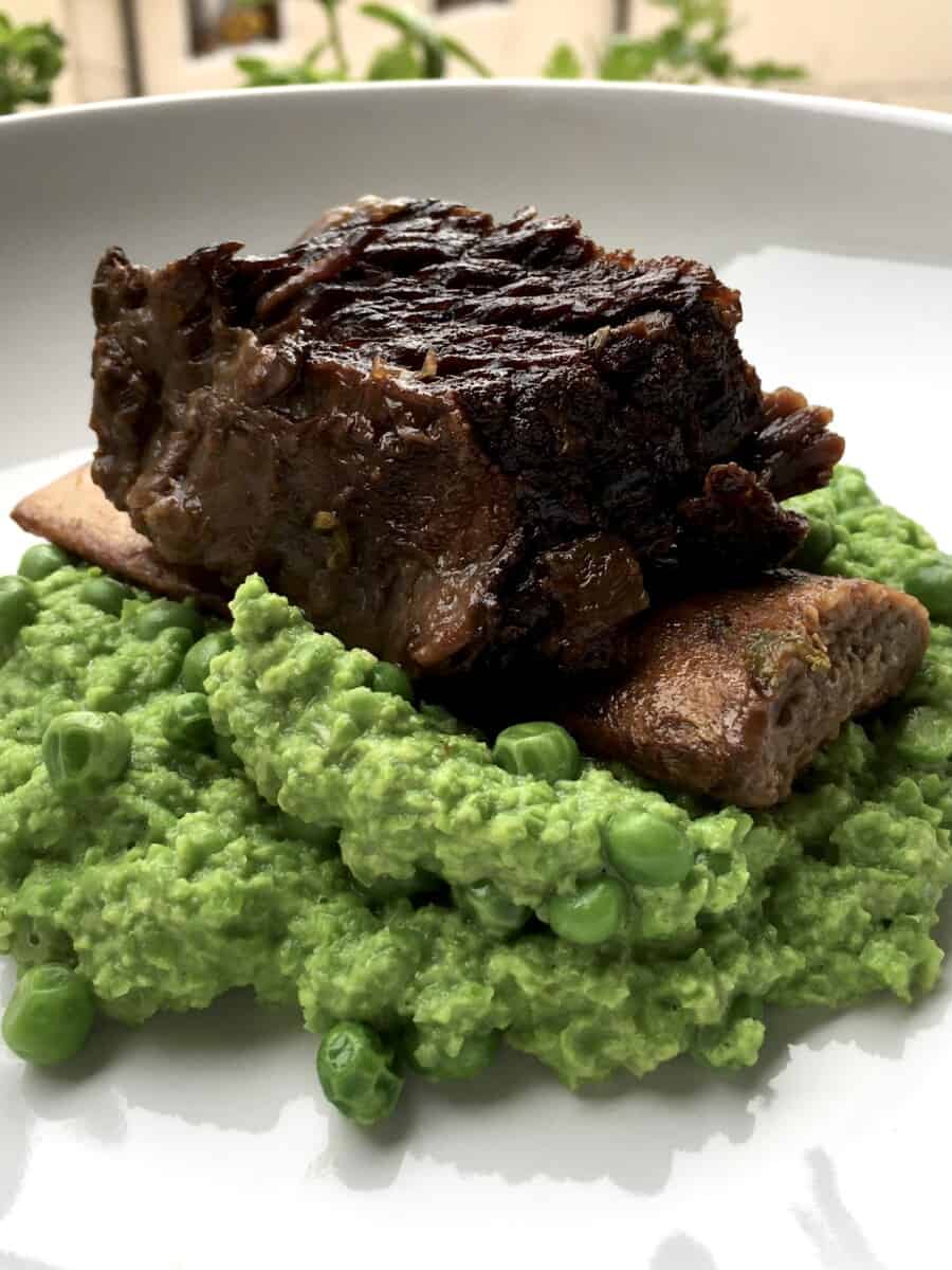 a single braised bone-in beef short rib sitting on top of a mound of bright green mushy peas