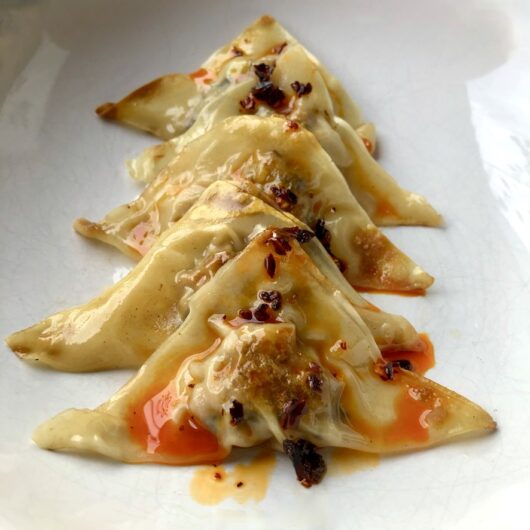 chinese potstickers layered in a row in a white ceramic dish with crispy chili oil drizzled on top