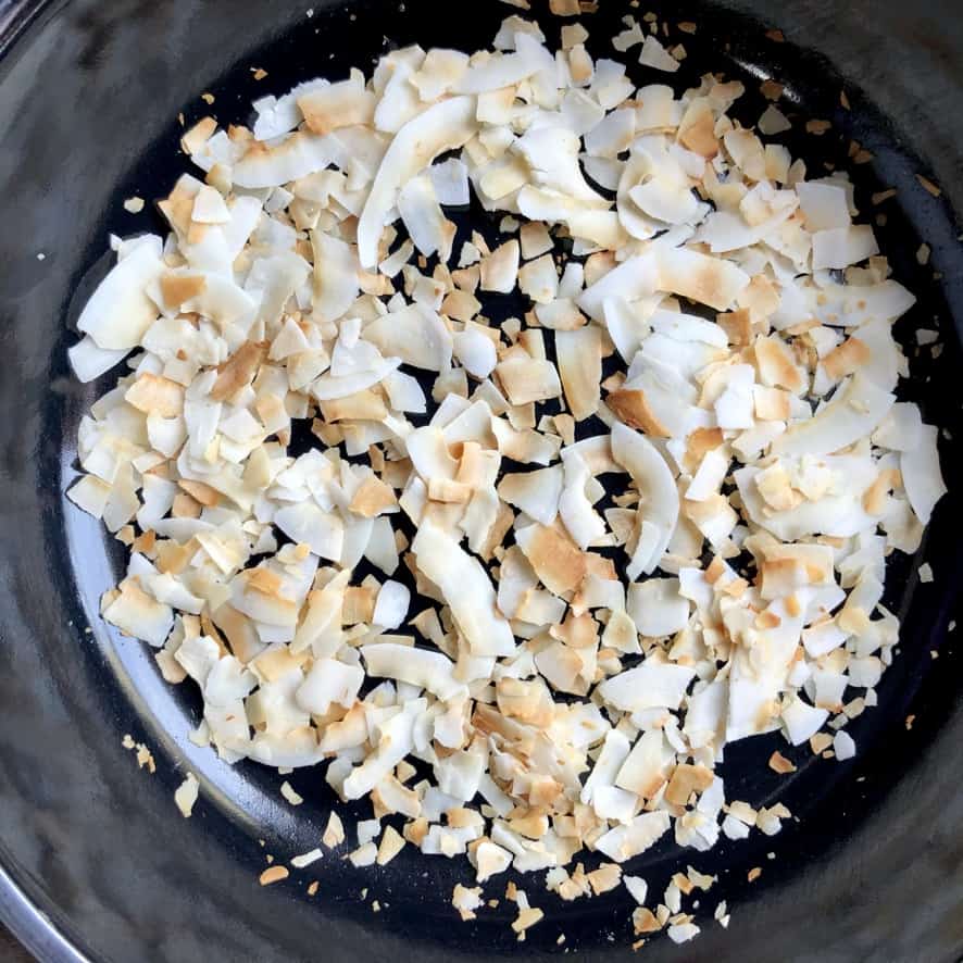 Toasted large coconut flakes in a saute pan.