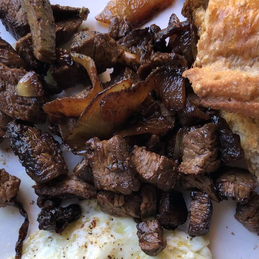 carne asada and caramelized onions with a little crusty bread and fried eggs in view