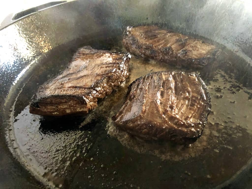 pan-searing carne asada steaks in a cast iron skillet
