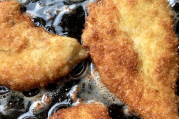 chicken breast cutlets being shallow-fried in extra virgin olive oil in a cast iron skillet