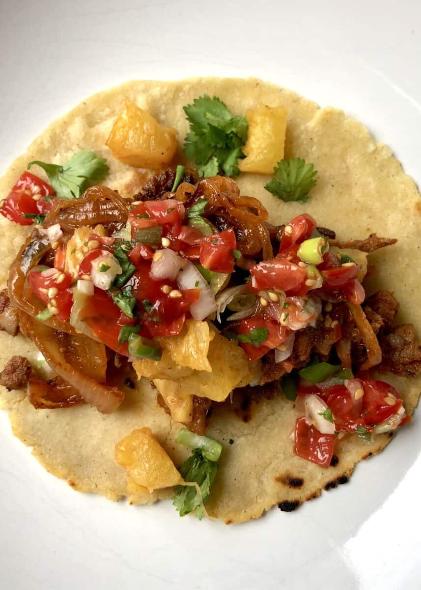 tacos al pastor on a homemade white corn tortilla with grilled pineapple and salsa
