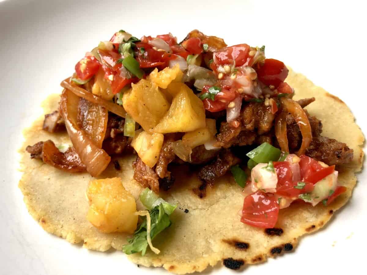 tacos al pastor on a homemade white corn tortilla with grilled pineapple and salsa
