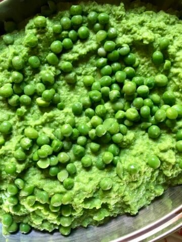 A serving platter filled with bright green creamy mashed sweet mushy peas with whole sweet peas for garnish.