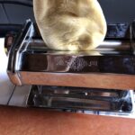 placing a piece of dough into the pasta machine for the first round of rolling on the widest setting