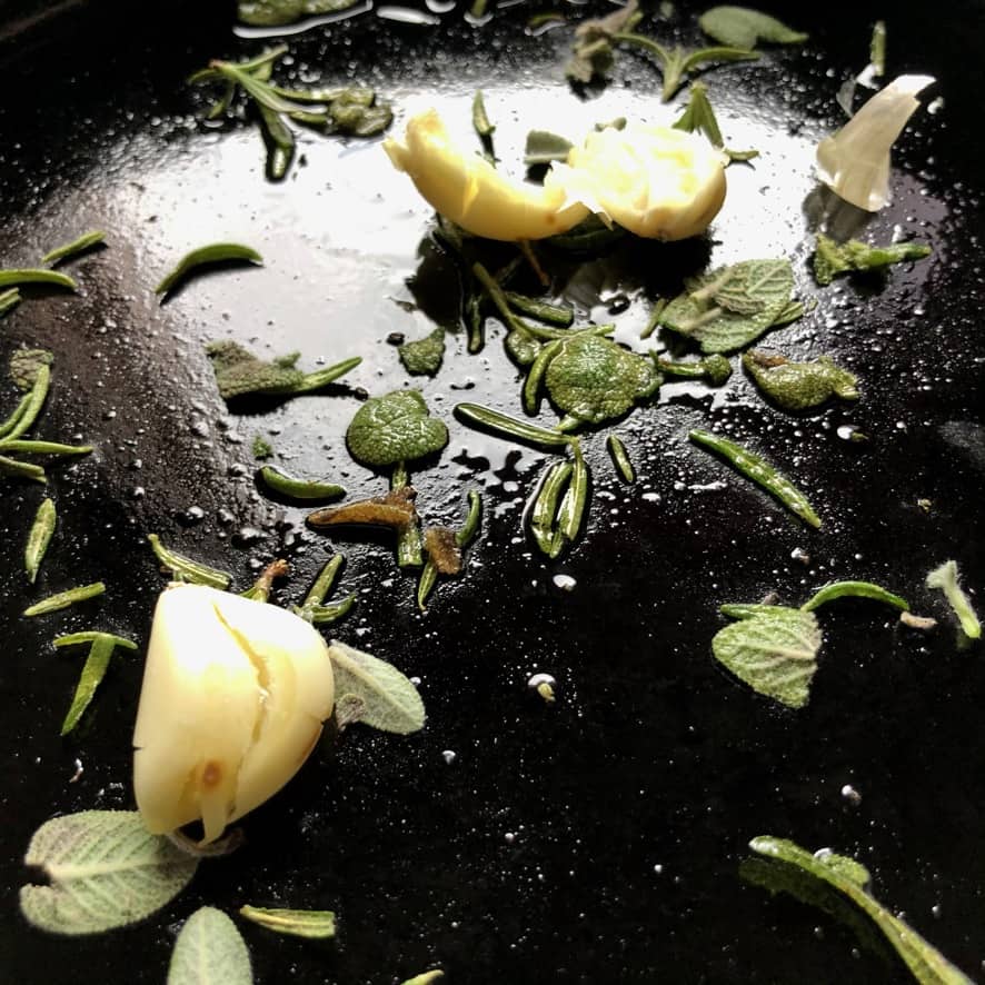 sage, rosemary and garlic cloves in a cast iron skillet with extra virgin olive oil