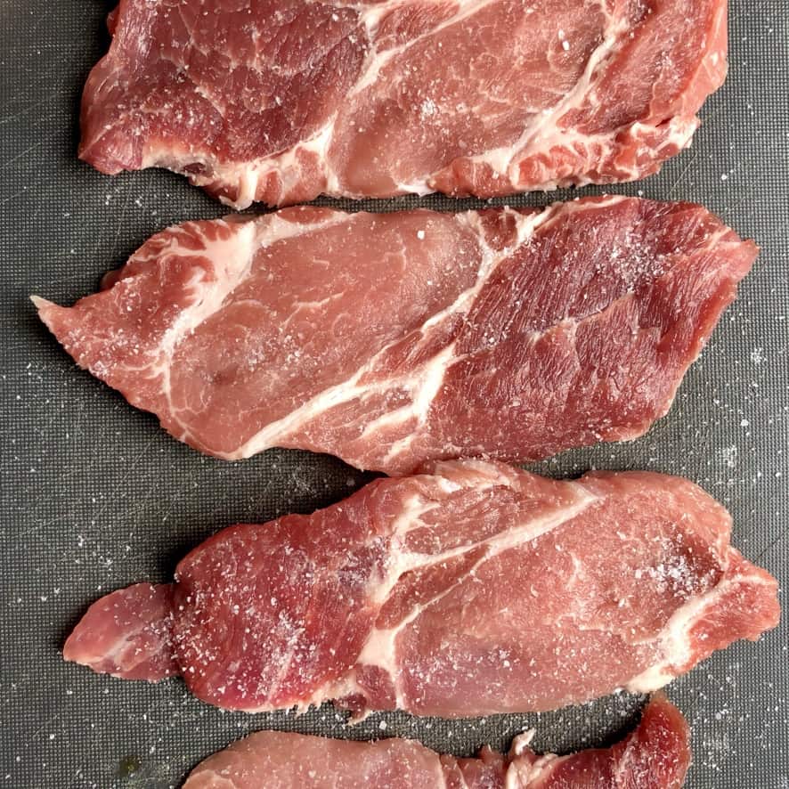 4 raw pork shoulder steaks on a cutting board
