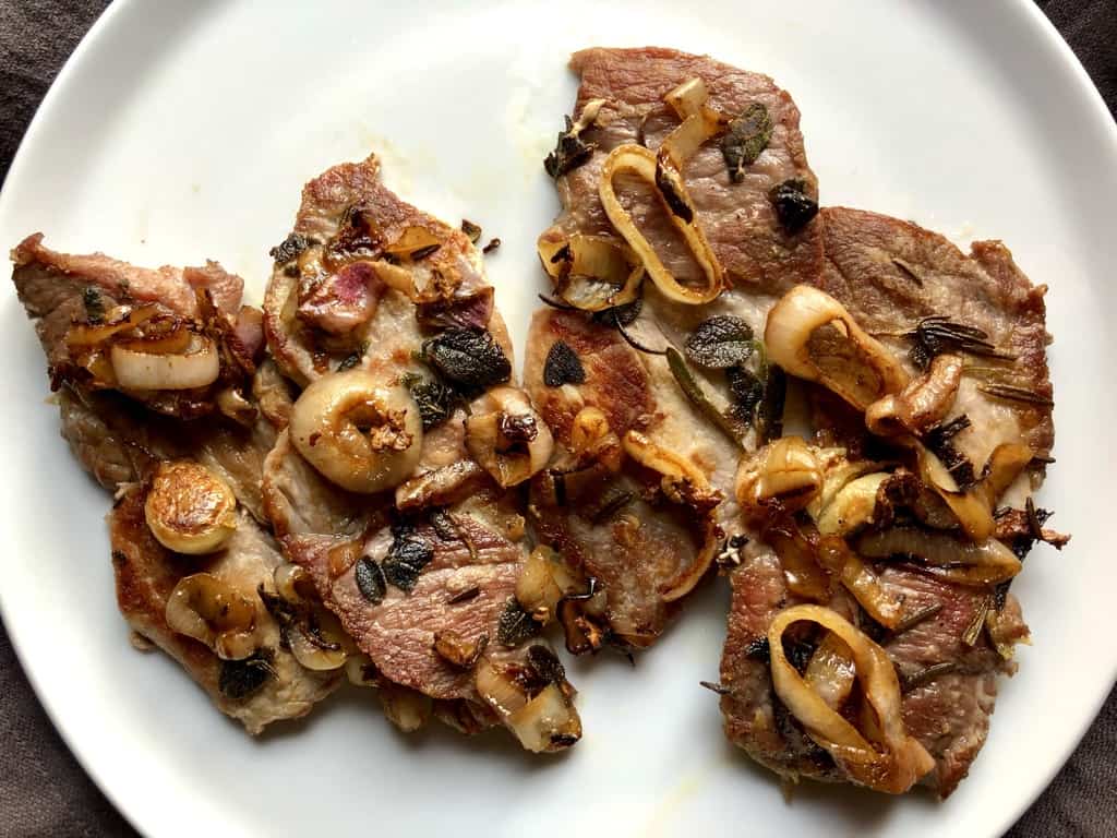 beautifully golden brown pork steaks with herbs and caramelized shallots on top on a white platter