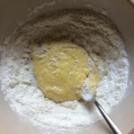 starting to incorporate the whisked eggs into the flour a little more as the mixture is coming together and changing from a dark yellow color to a butter yellow color