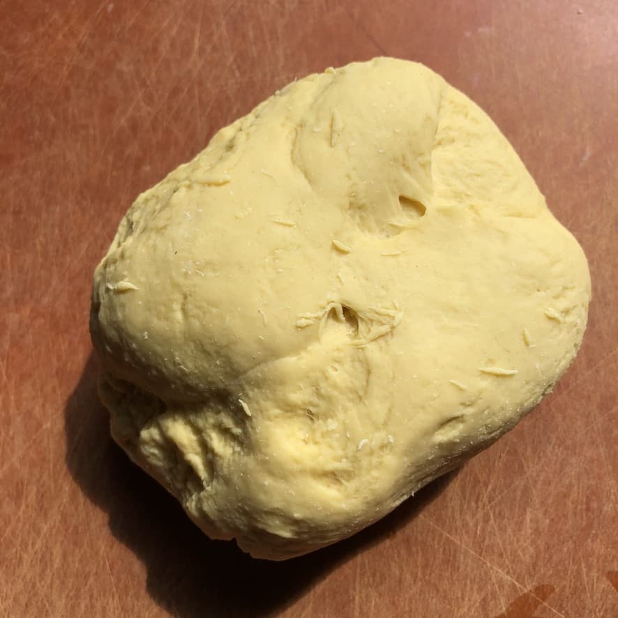 an unformed piece of fresh egg pasta that is much smoother than when it was first made showing it has been kneaded the right amount, but still needs to be formed into a ball
