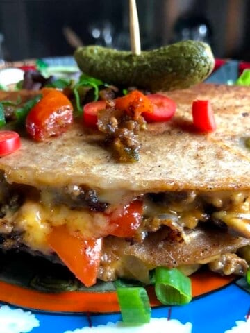 Sliced and stacked melty ooey gooey cheeseburger quesadillas with a speared pickle on top.