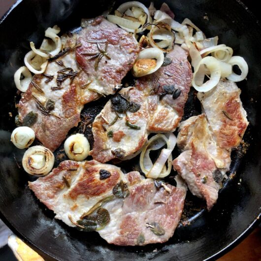 pan seared pork steak in a cast iron skillet with shallots, garlic, and herbs
