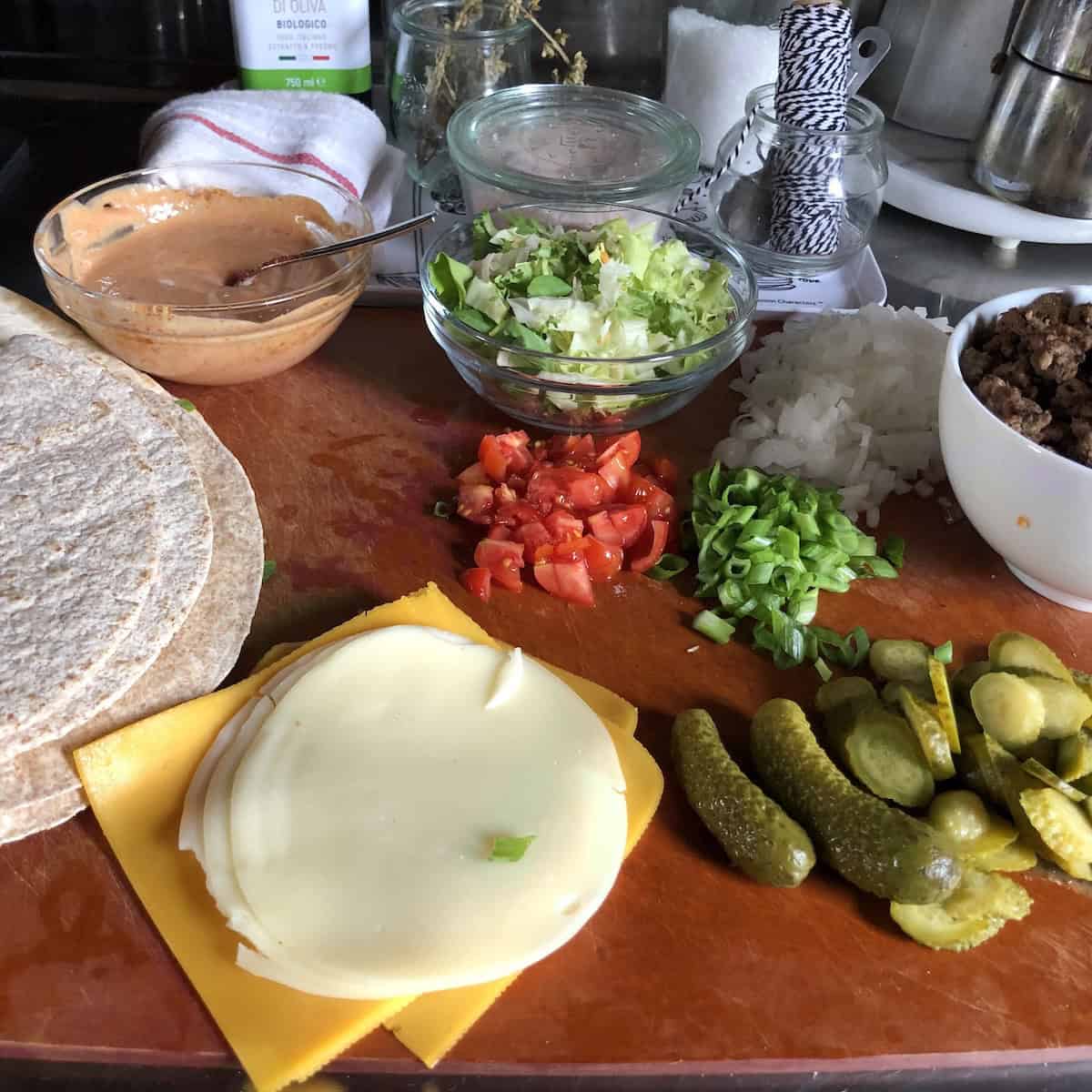 Mise en place for cheeseburger quesadillas on a cutting board ready to assemble.