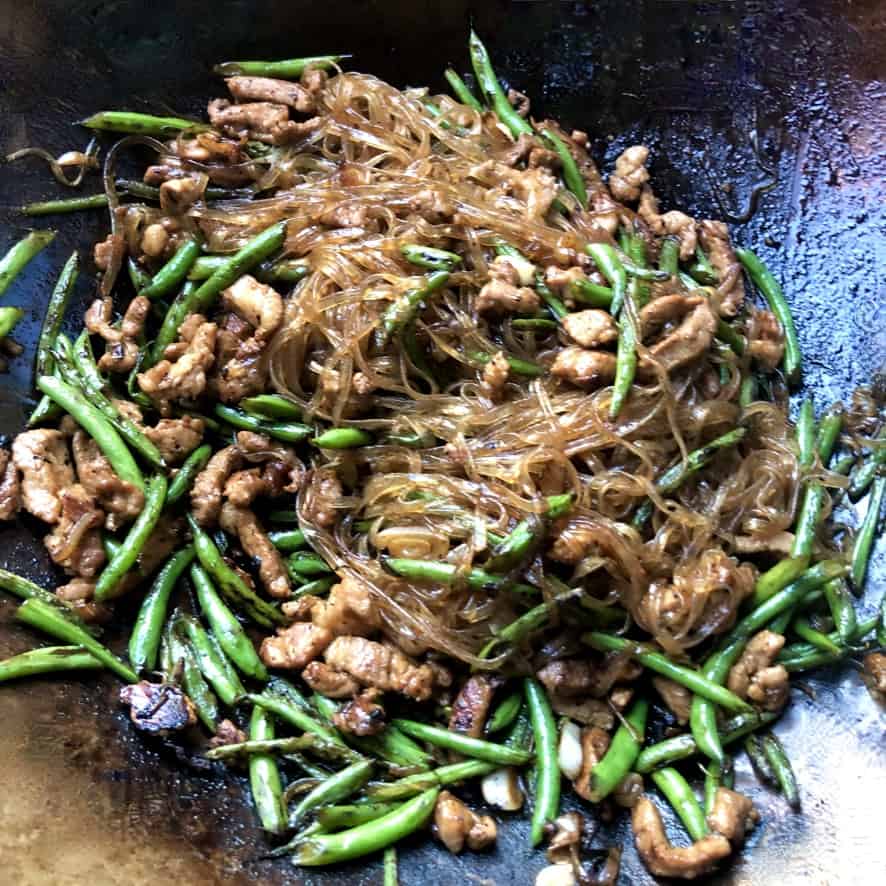a wok filled with beautifully brown glass fettuccine noodles, tender slivers of pork and garden fresh green beans