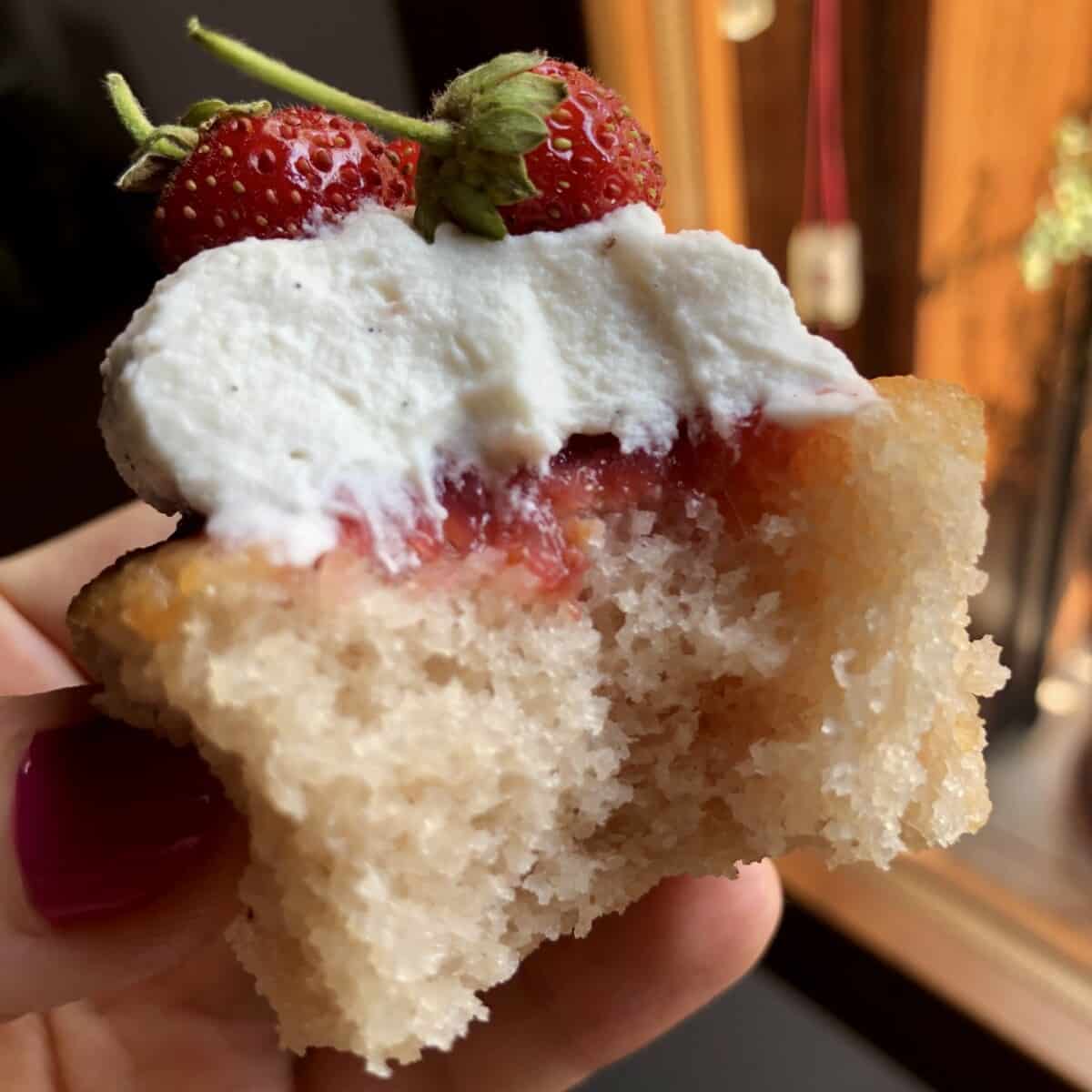 a single strawberry cupcake with strawberry gelée, strawberry vanilla bean whipped cream and baby wild Italian strawberries as garnish with a bite taken out revealing the super tender crumb.