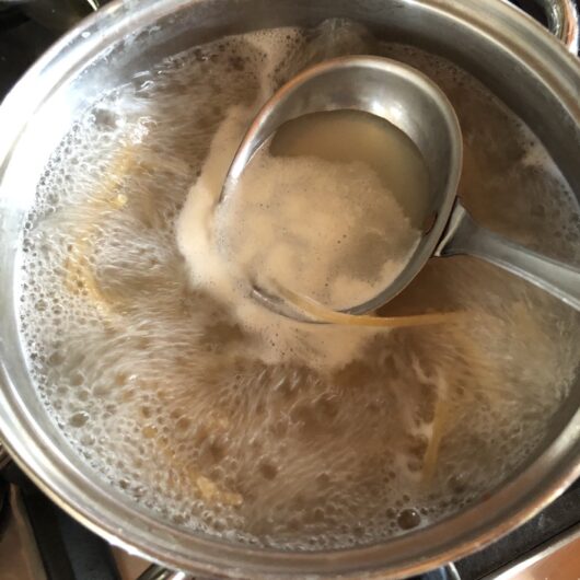 a ladle removing some starchy past water about to be added to the sauce