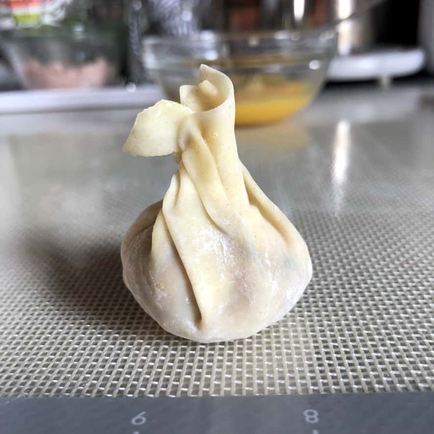 a money bag wonton sealed just before tying a scallion tie around it to close it up