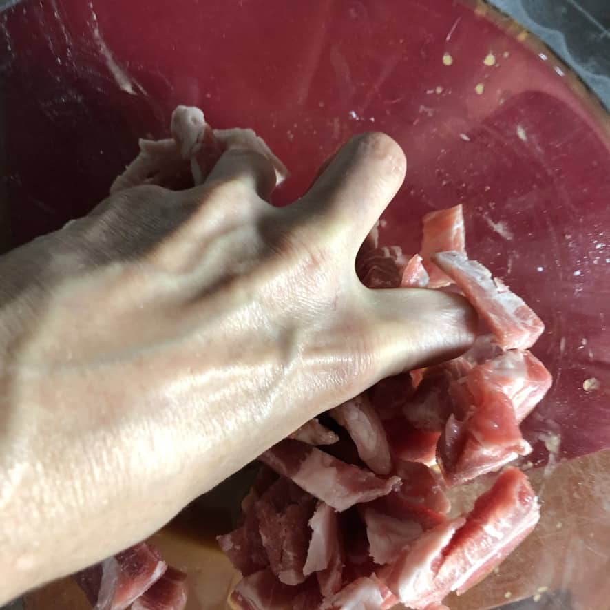 my hand massaging the pork and velveting mixture in a mixing bowl