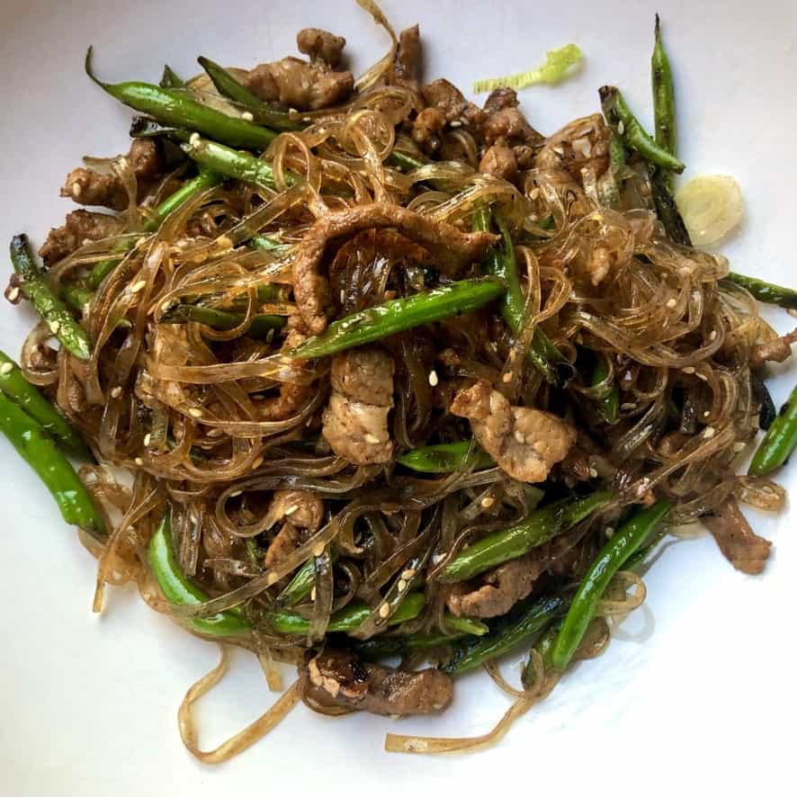 closeup of a pasta bowl filled with a wok filled with beautifully brown glass fettuccine noodles, tender slivers of pork and garden fresh green beans