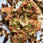 pan seared soy ginger salmon sprinkled with scallions, toasted sesame seeds and crispy salmon skin slivers with caramelized shallot halves resting on top