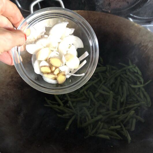 adding the aromatics (garliic, scallions, and ginger) to the wok with the green beans