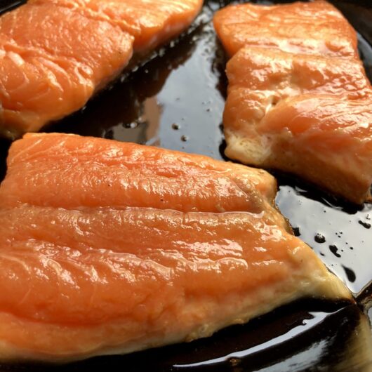 3 salmon filets cooking in a well seasoned cast iron skillet with EVOO