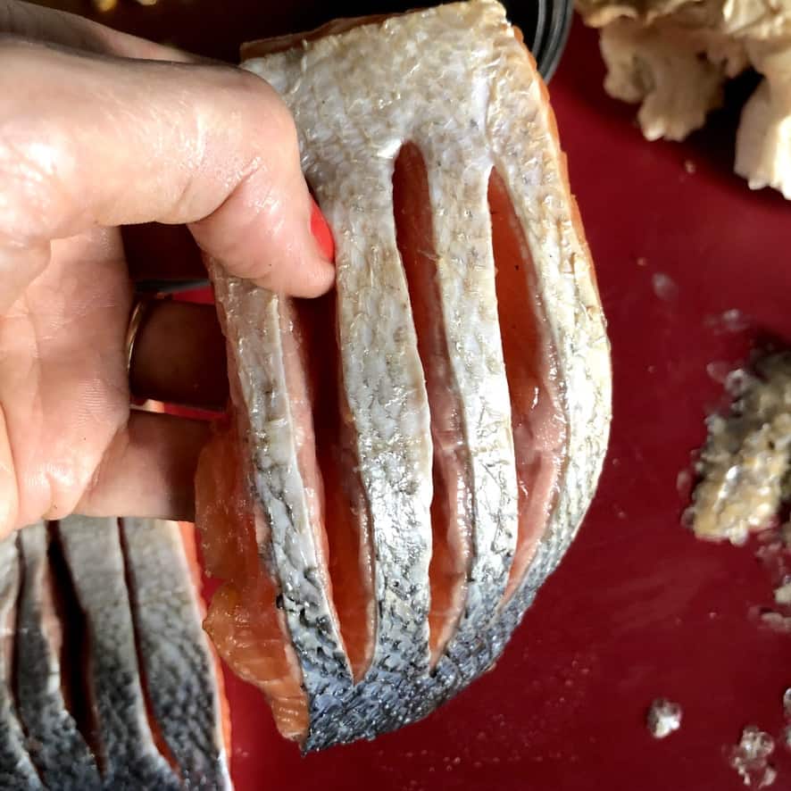 my hand holding up the cut salmon filet revealing the 3 slits I made in the skin-side in order to season the inside