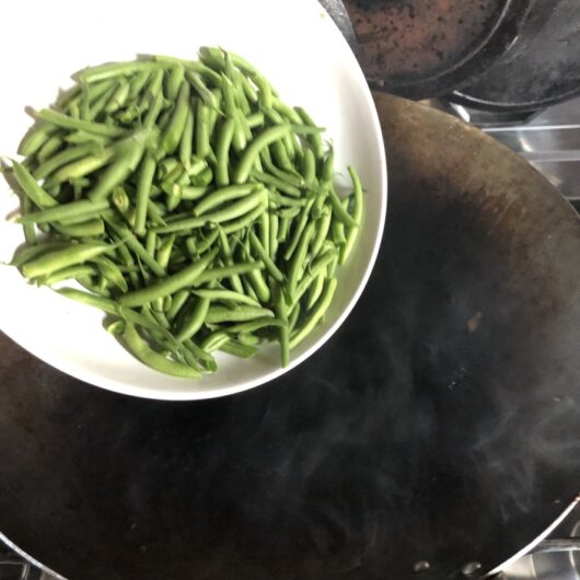 adding sliced green beans to the wok to cook