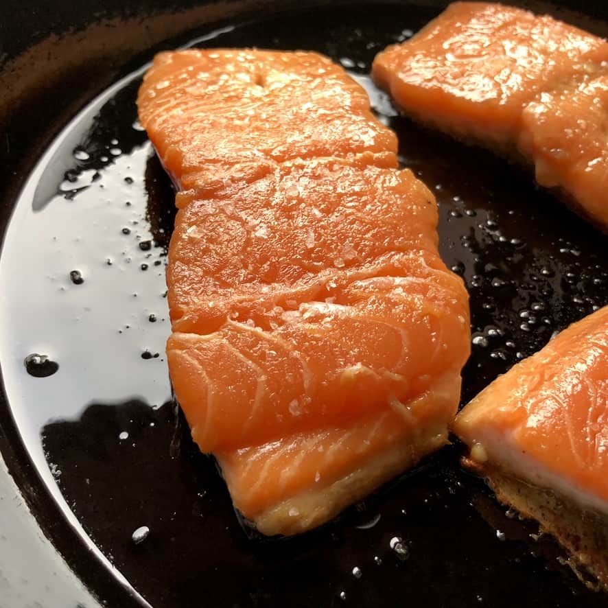 3 salmon filets cooking in a well seasoned cast iron skillet with EVOO