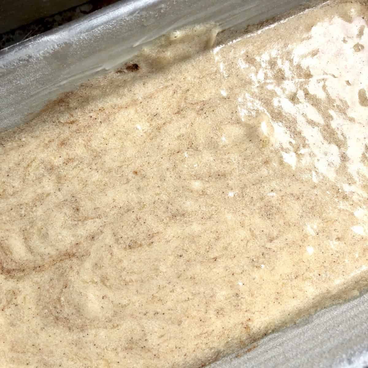 Dark banana bread batter in a loaf pan from the pumpkin pie spice, waiting for the pumpkin seed crunch topping to be added before baking.