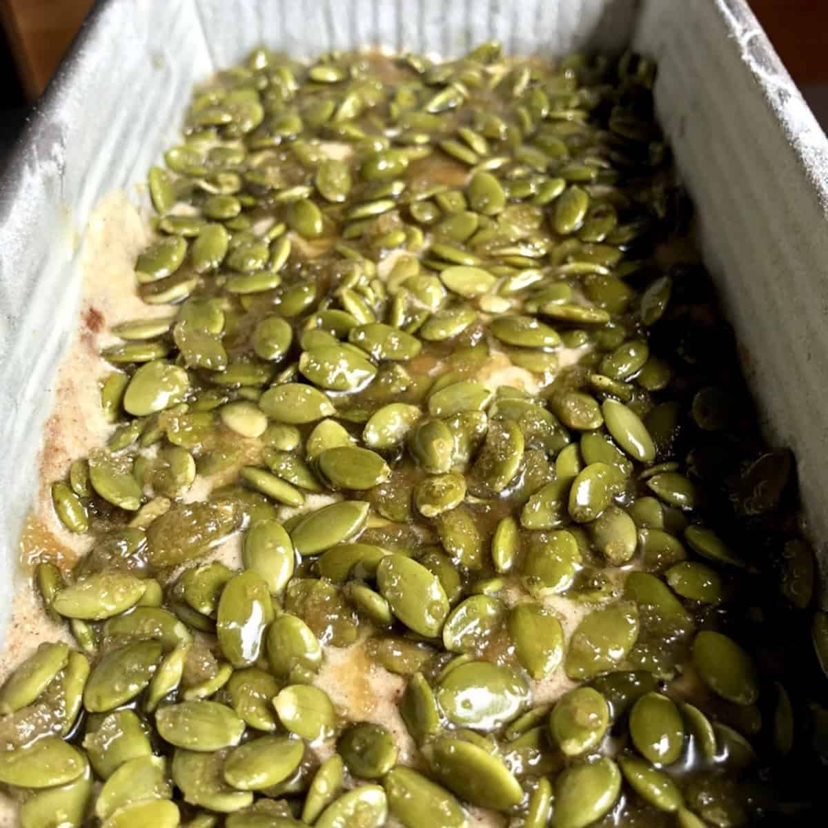Pumpkin spice banana bread batter in a loaf pan topped with pumpkin seed crunch ready to bake.