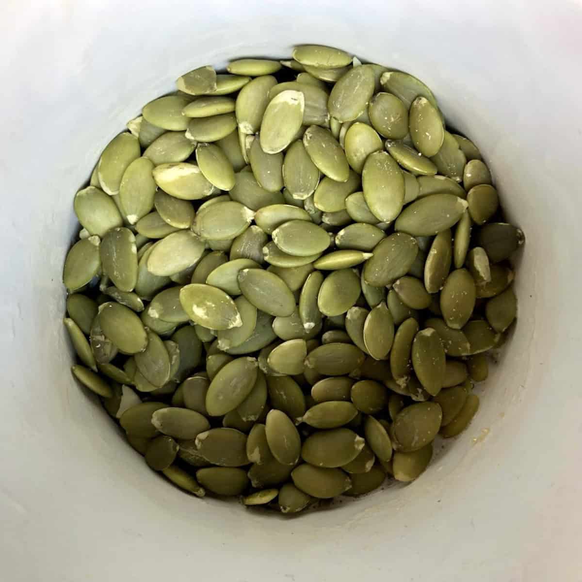 Green raw hulled pumpkin seeds pepitas in a bowl showing the right kind of pumpkin seeds for baking (like pumpkin bread, banana bread, etc.)
