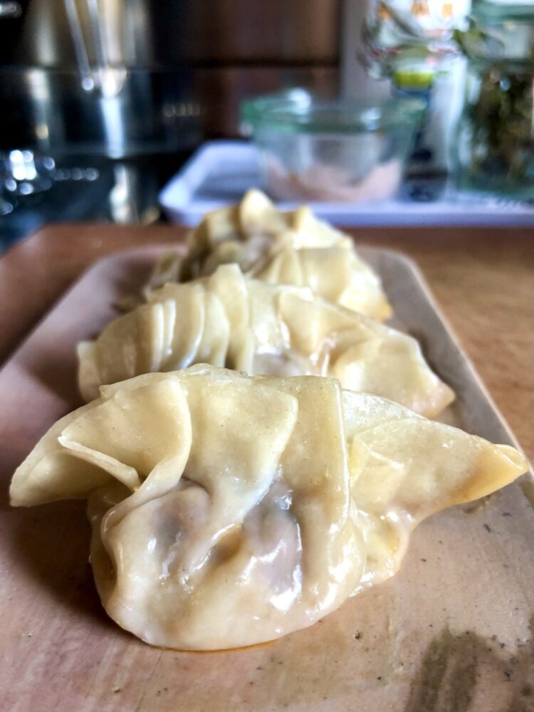 Just steamed homemade dumplings on a pink marble rectangular serving tray glistening and looking delicious and ready to eat