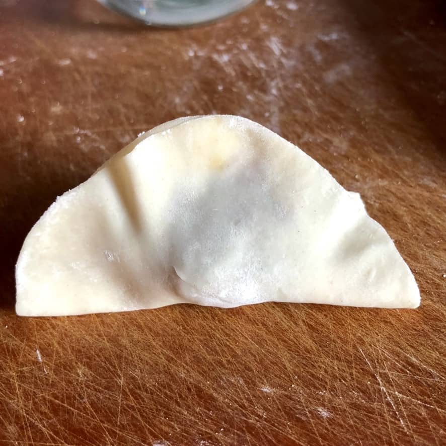 a filled and half-sealed chicken dumpling (in a half-moon shape)