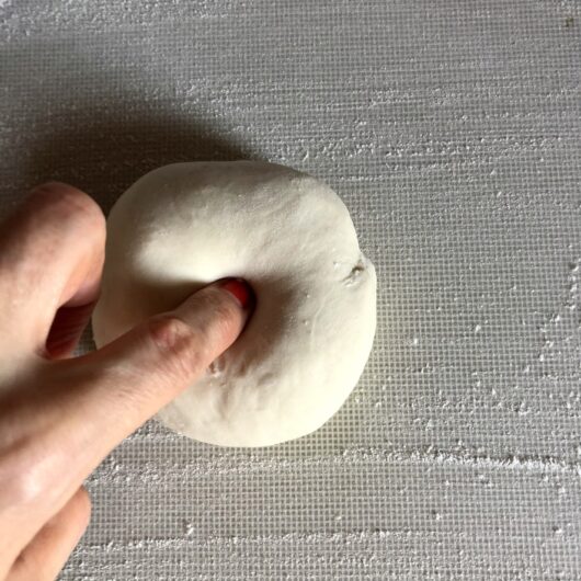 me pressing my finger into the center of the dough to make a hole in order to get the dough "log" needed to start pinching off dough for individual dumplings