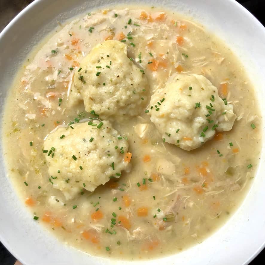 A bowl of chicken and dumplings with 3 fluffy dumplings in the middle surrounded by chunks of chicken and vegetables.