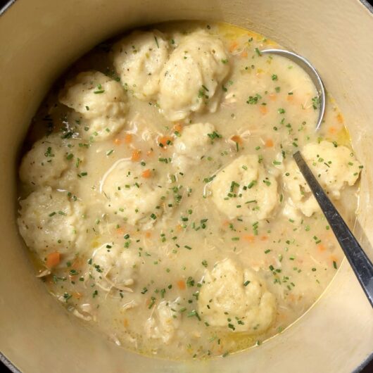 a le creuset 7-quart dutch oven filled with chicken and dumplings soft and pillowy and floating on top with chives sprinkled all over