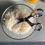 a pair of scissors sitting inside the mixing bowl with the glass noodles after being cut into shorter pieces