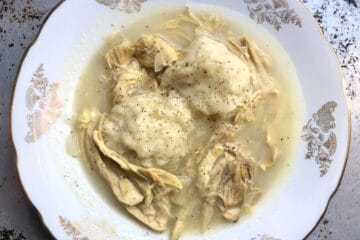 A bowl of simple chicken and dumplings with two dumplings surrounded by creamy chicken soup.