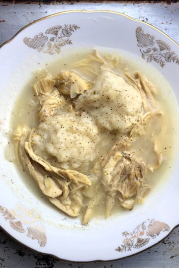 A bowl of simple chicken and dumplings with two dumplings surrounded by creamy chicken soup.