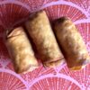 3 super golden brown crispy spring rolls on a pink and peach tray decorated with Chinese fans