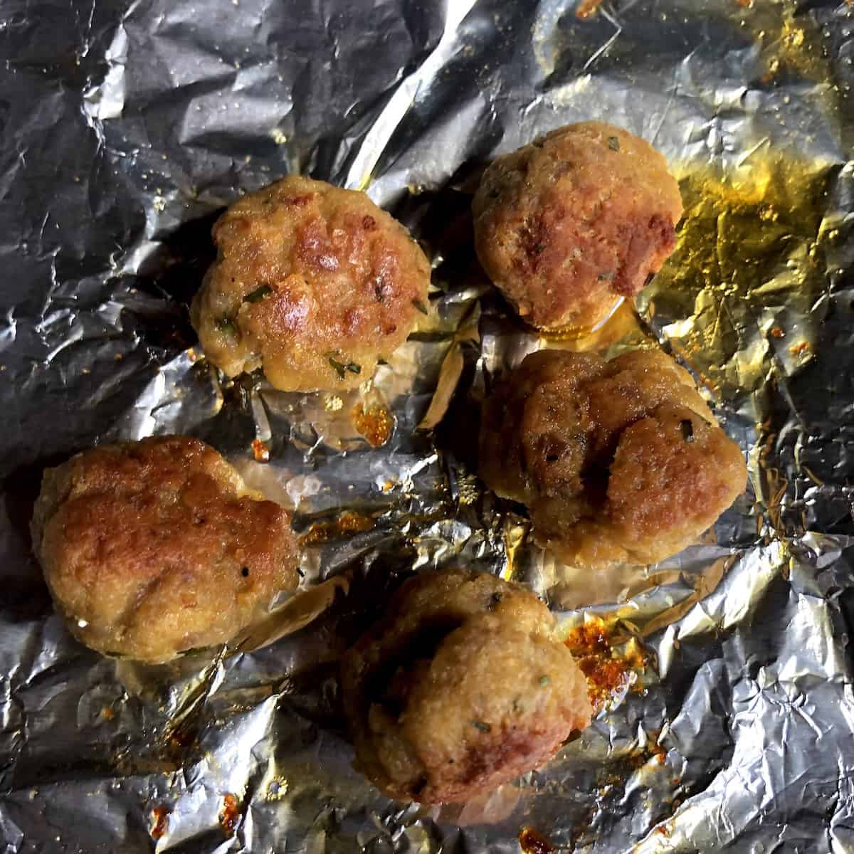 Golden brown baked chicken and pork meatballs fresh from the oven on a sheet pan for tender juicy homemade meatball recipe.