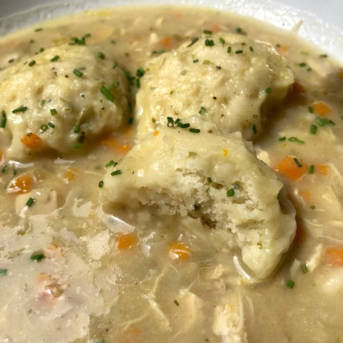 A bowl of chicken and dumpling soup with a drop dumpling broken open showing the fluffy interior.