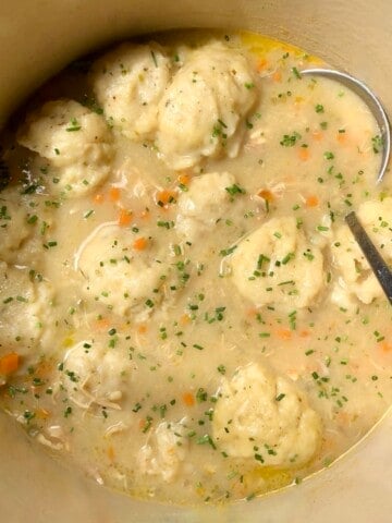 A pot of chicken and dumplings soup with fluffy drop dumplings garnished with chopped parsley ready to serve.